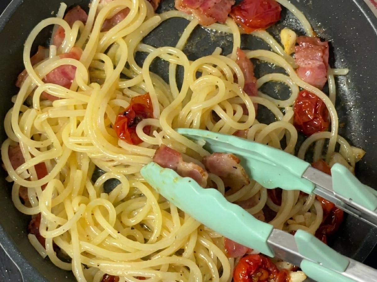 Black pepper being freshly ground over cooked pasta in a pan.