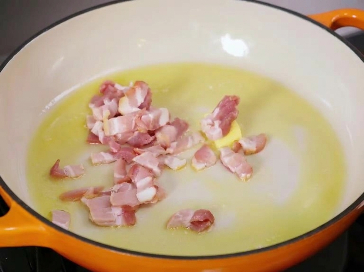 Diced pieces of raw bacon sizzling in a warm pan with melting butter and olive oil.