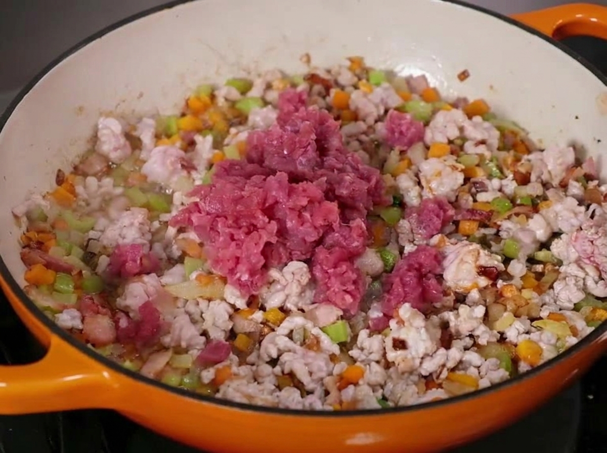 Ground beef and pork cooking with diced vegetables in a large enameled cast iron pan.