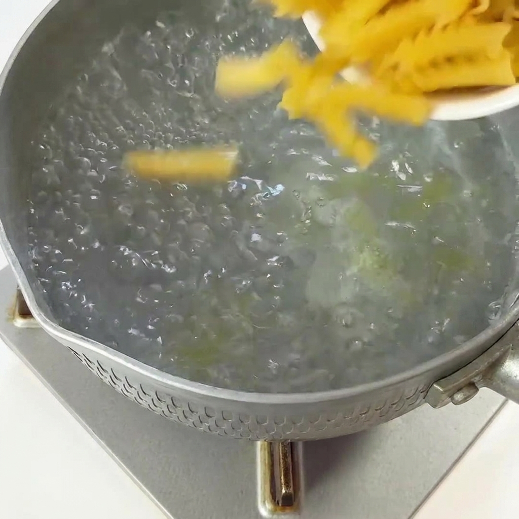 Dry fusilli pasta being poured from a small dish into a pot of boiling water.