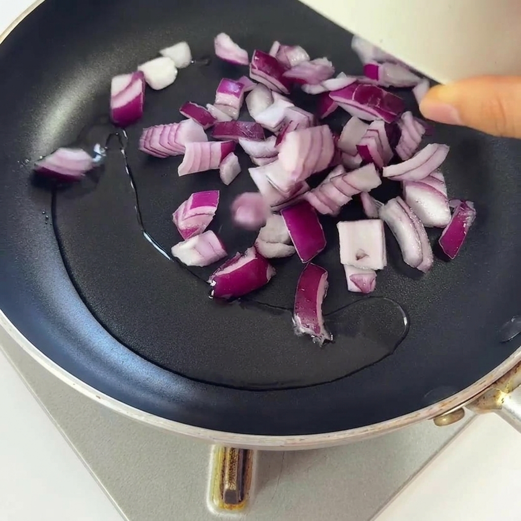 Chopped red onions frying in a pan with shimmering hot oil.