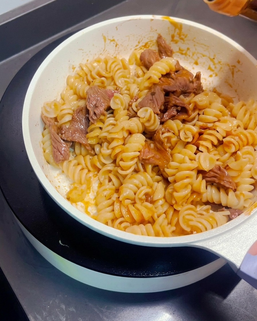 Dark soy sauce being drizzled over the stir-fried pasta and beef.