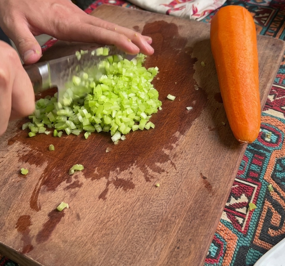 Finely diced celery and carrots sitting on a wooden cutting board next to a whole carrot.