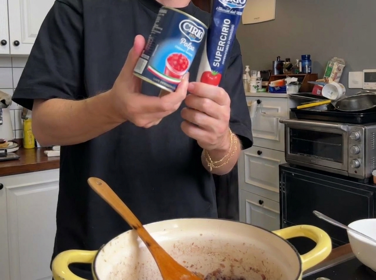 Canned tomato puree and a tube of tomato paste held above the cooking pot.