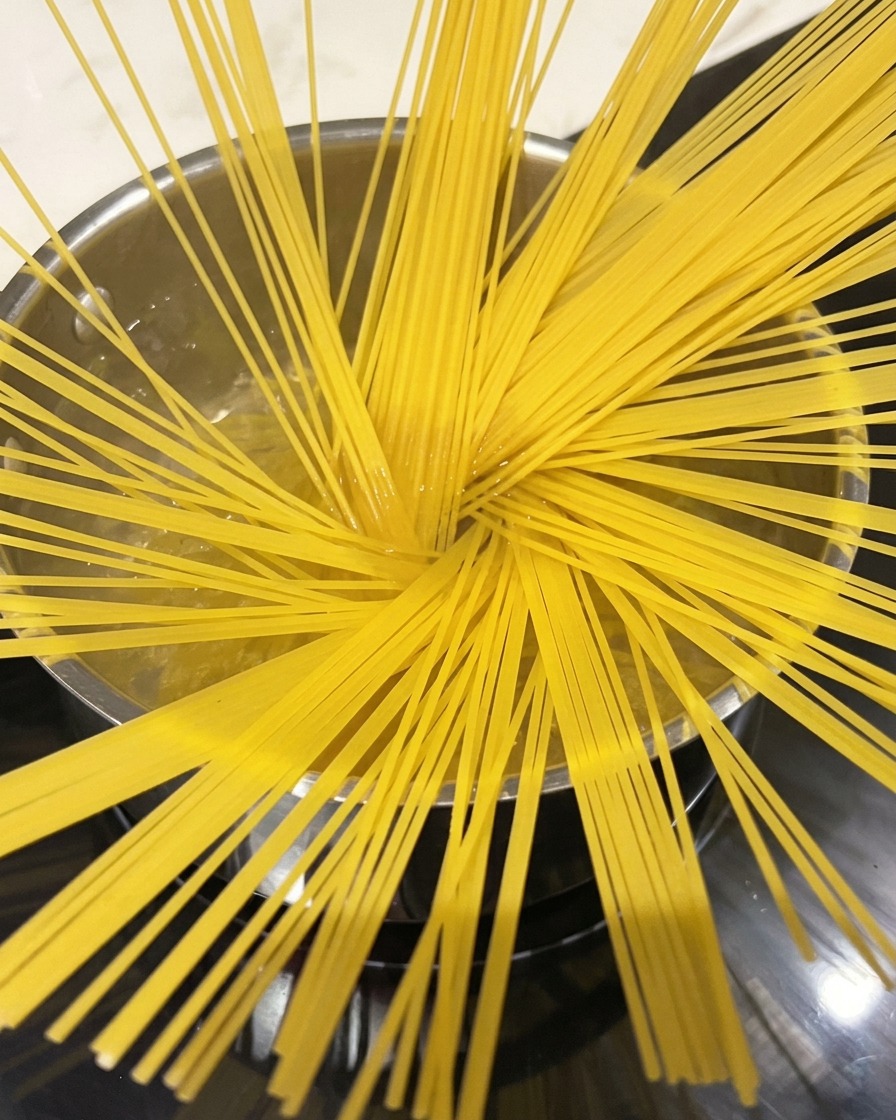 Spaghetti noodles boiling in a large pot of water, steam rising.