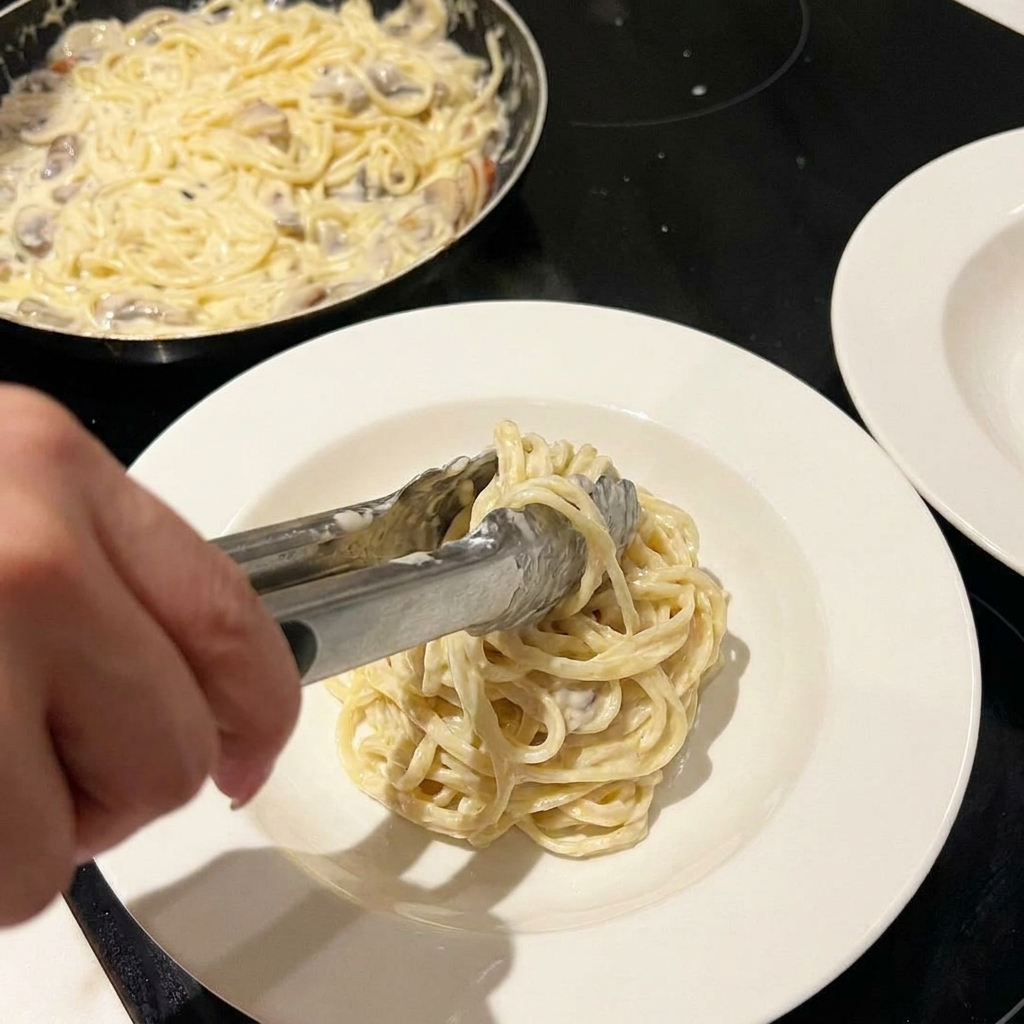 Creamy pasta being tossed in a pan with cheese and seasoning sprinkled on top.