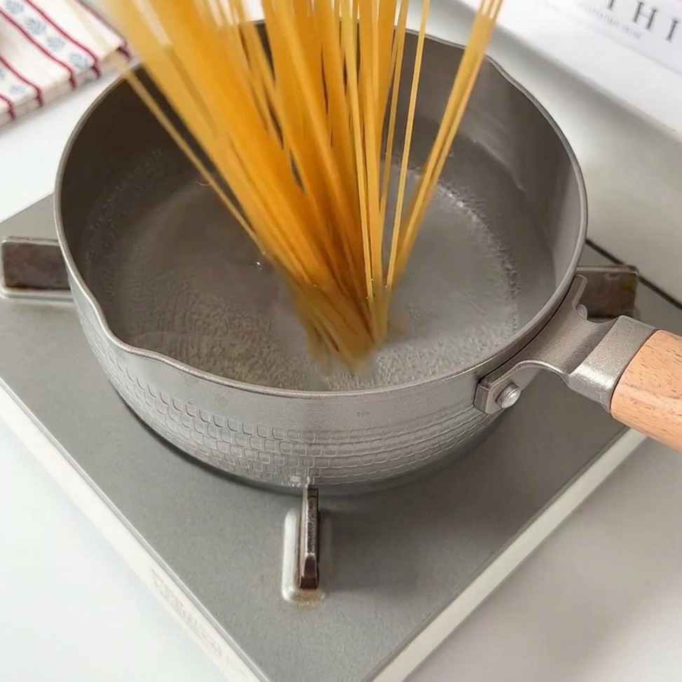 Long strands of spaghetti noodles being submerged into a pot of boiling water.