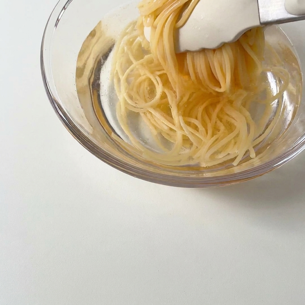 Cooked spaghetti being lifted with tongs and placed into a bowl of cold water.