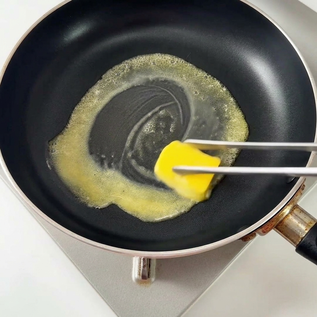 A square of butter melting in a hot black non-stick skillet.