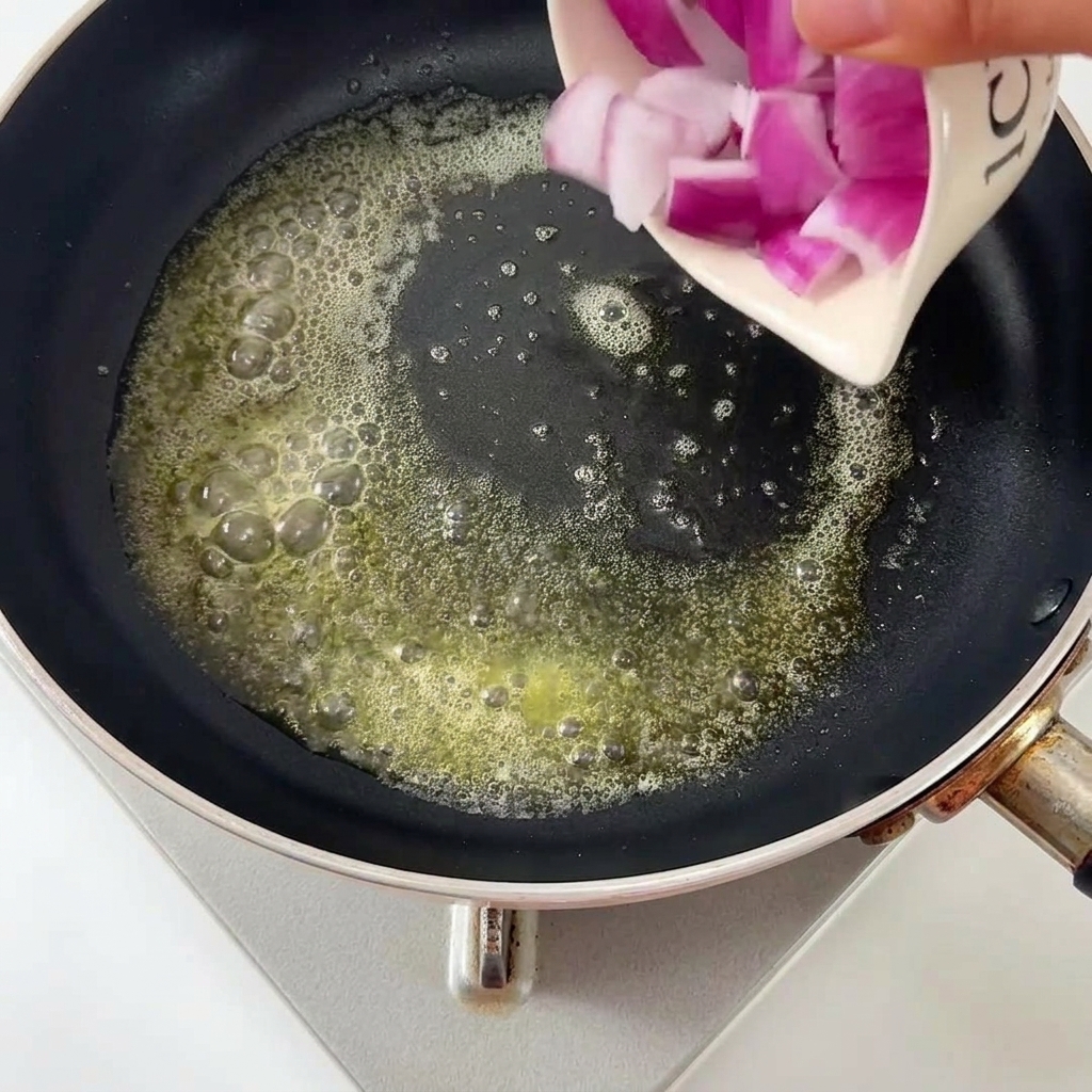 Diced red onions being poured into a frying pan with melted butter.
