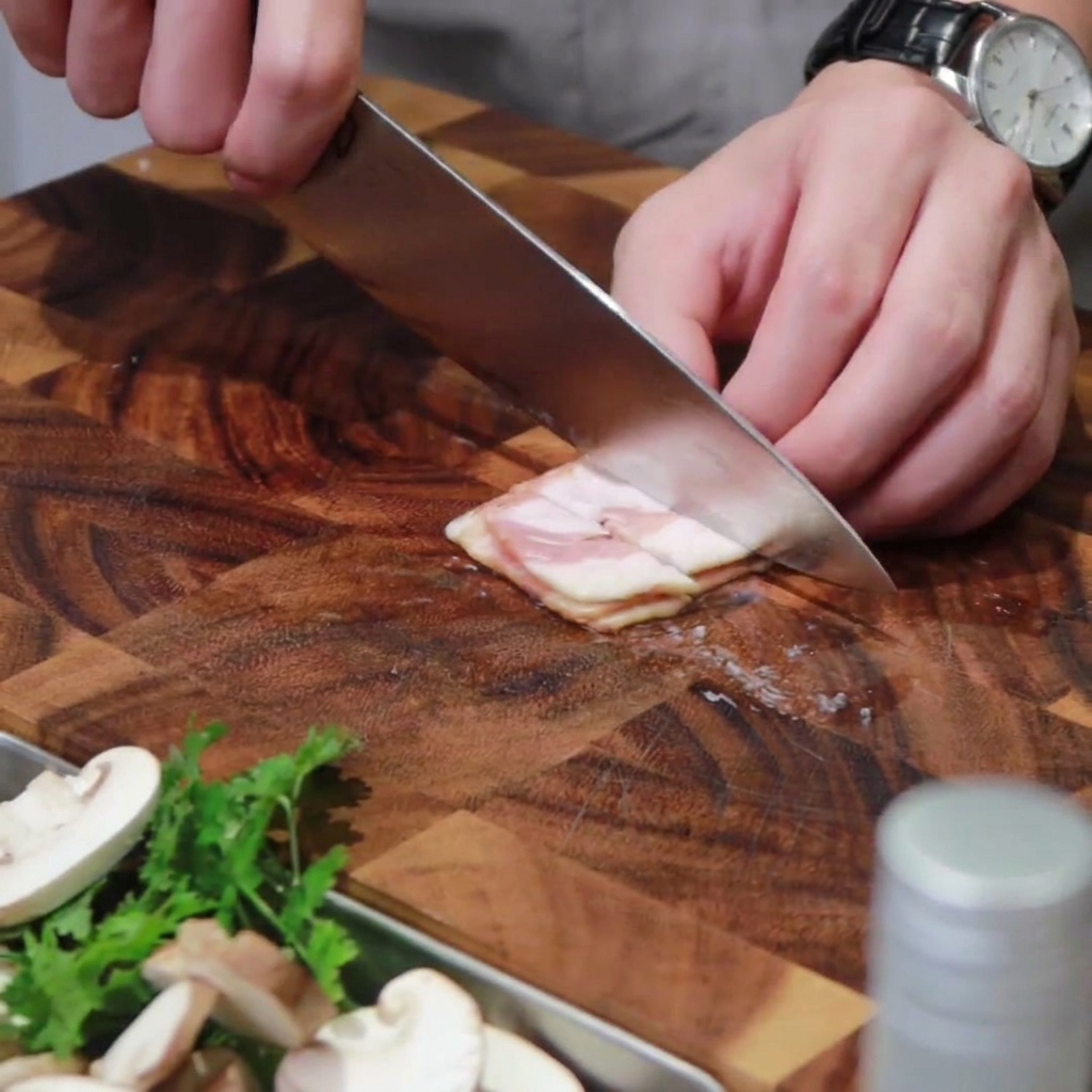 Slices of bacon being cut into segments on a wooden cutting board.
