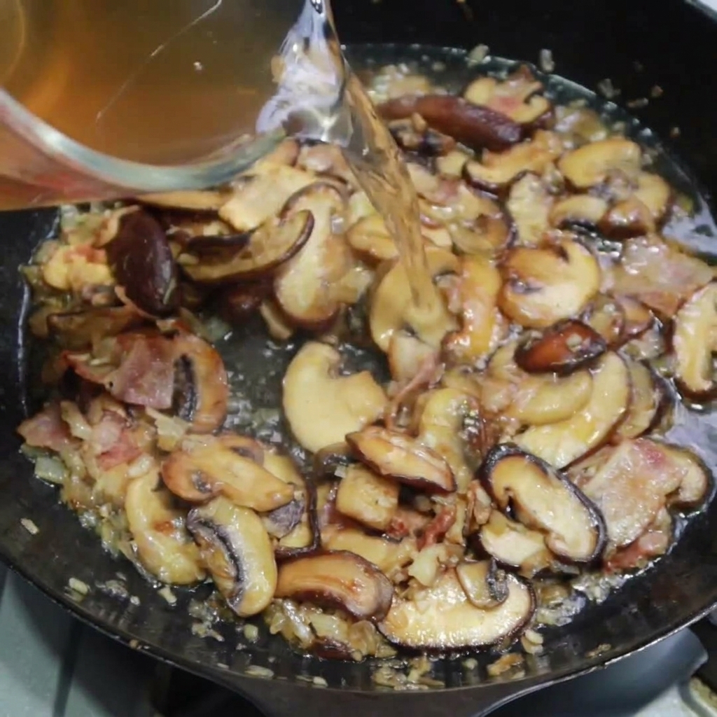 Chicken stock being poured into the pan to simmer with the bacon and mushroom mixture.