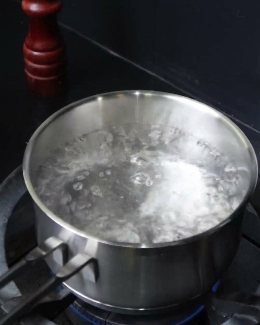 Spaghetti noodles being submerged into a pot of boiling salted water.