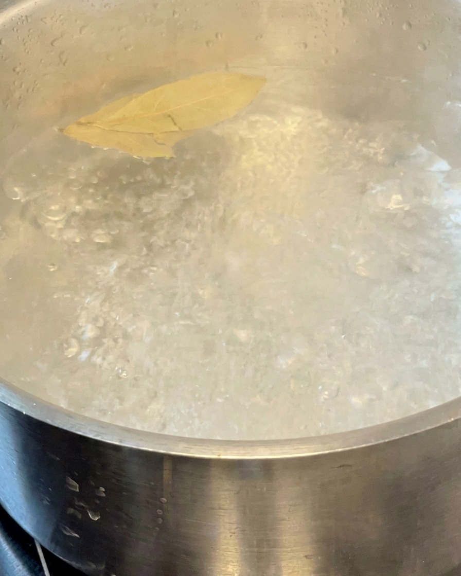 Pasta cooking in a pot of boiling water with two bay leaves floating on the surface.
