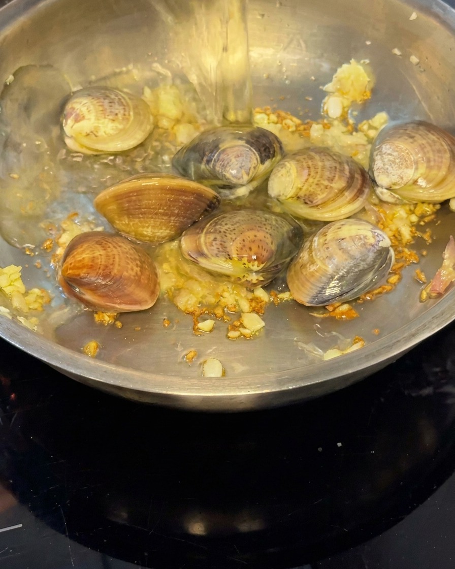 White wine being poured into the pan over the clams to create steam.