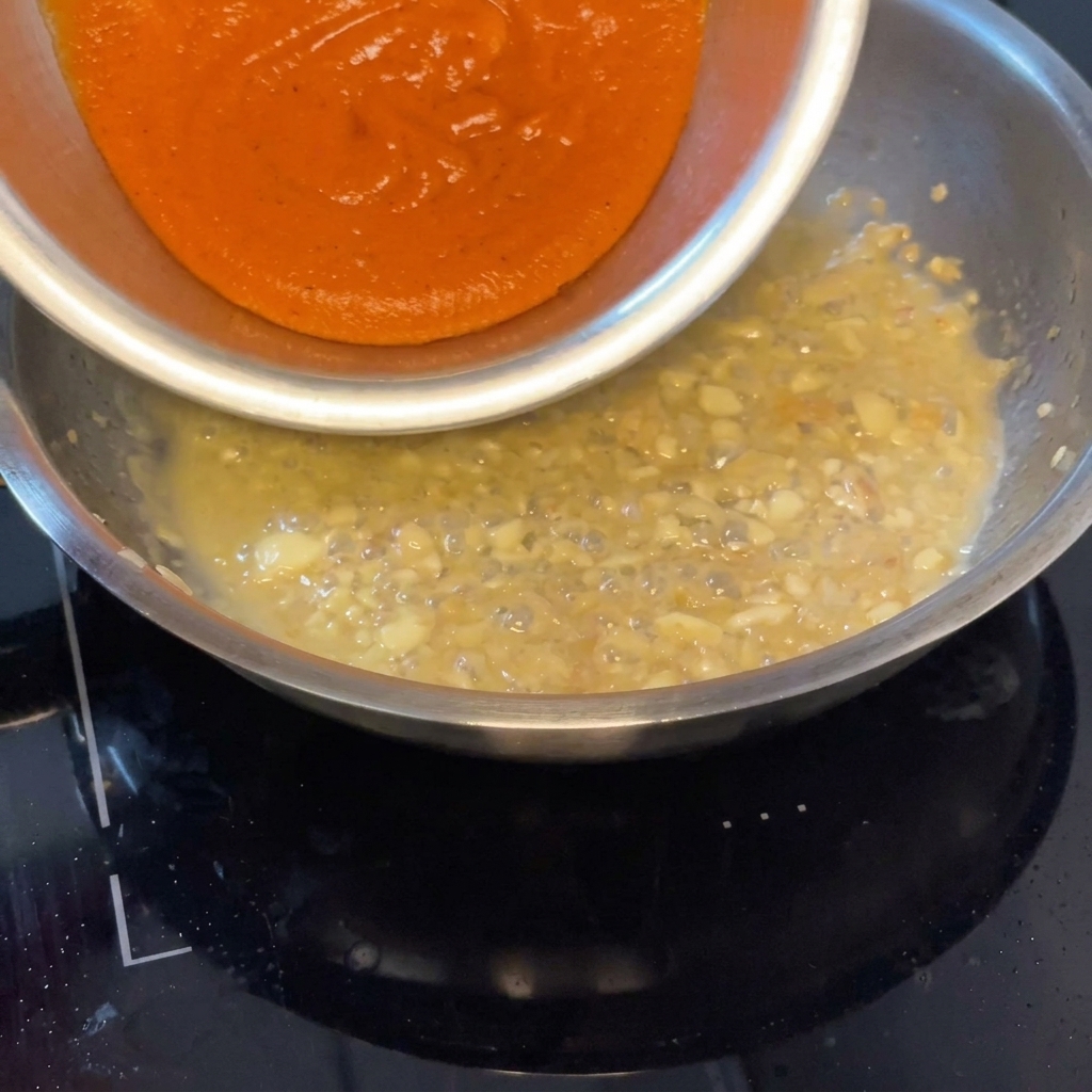 Roasted pepper sauce being poured into the pan to mix with the aromatic liquid.