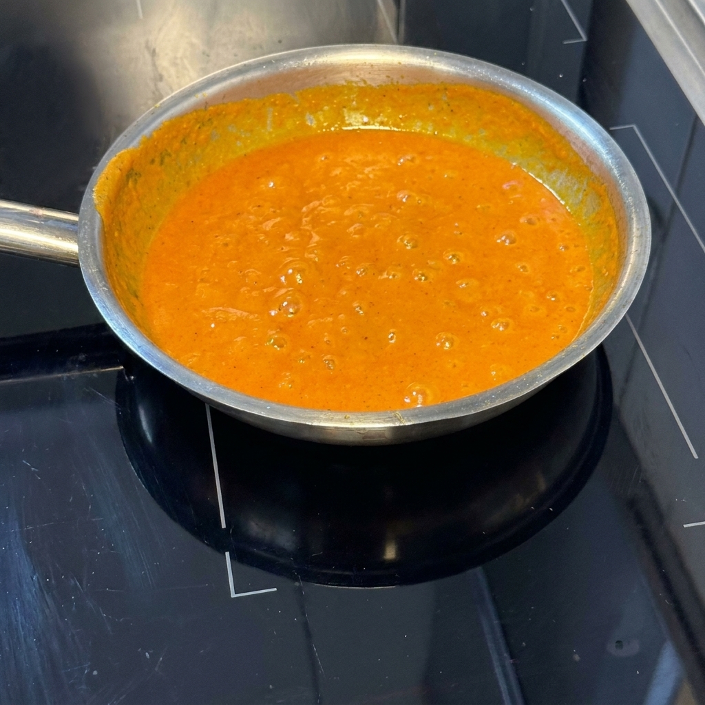 Cooked pasta strands being stirred into the vibrant orange roasted pepper sauce in the pan.