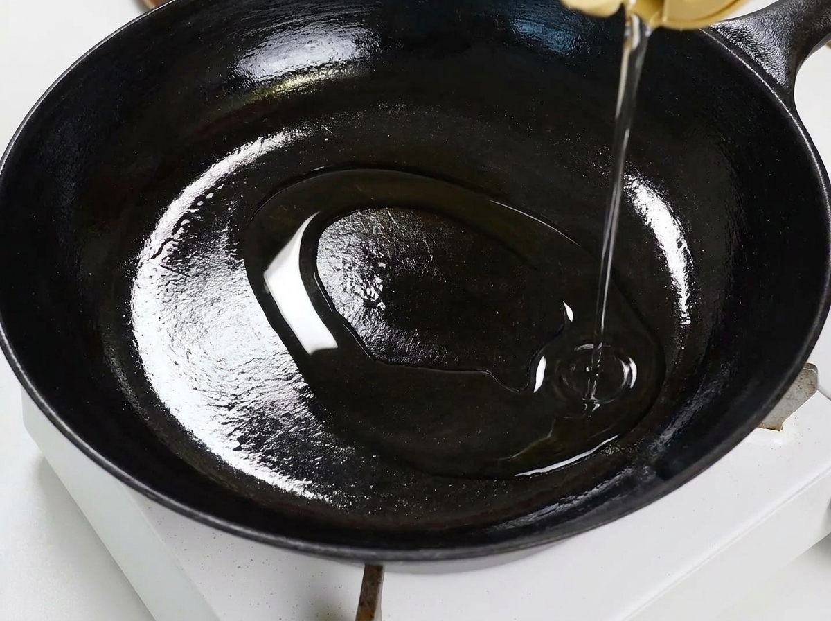 Slices of garlic and red chili flakes sizzling in oil in a flat black pan, being stirred with a wooden spatula.