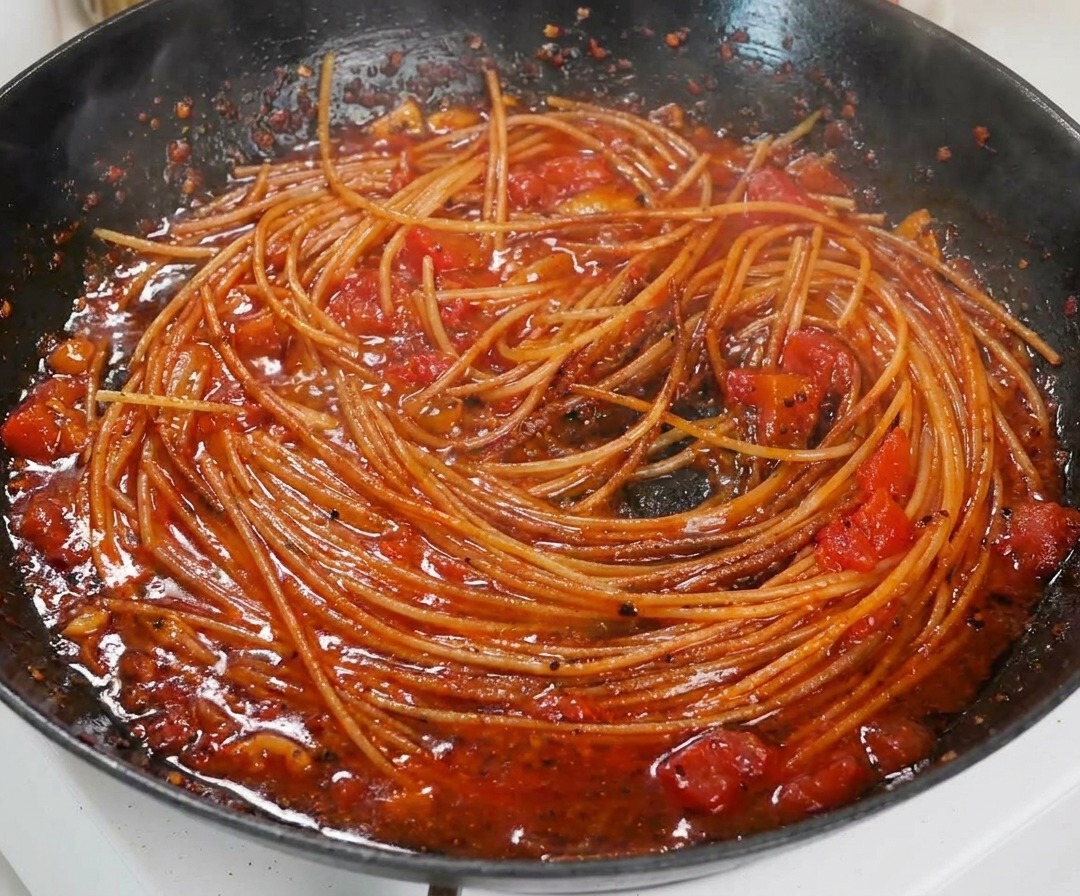 Close-up of cooked spaghetti tossed in a rich, thick tomato sauce in a black pan.