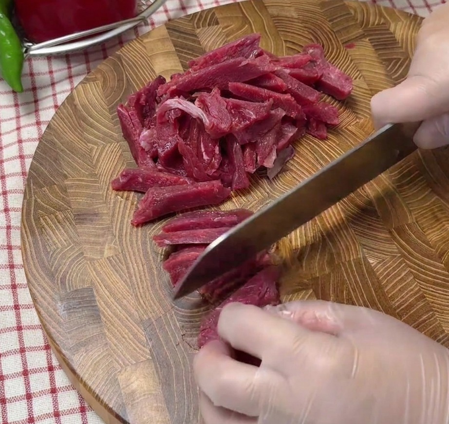 Thinly sliced raw beef strips neatly arranged on a wooden cutting board.