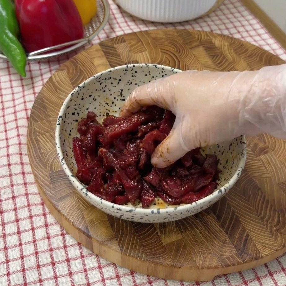 Raw beef strips being marinated in a speckled bowl with soy sauce and seasonings.