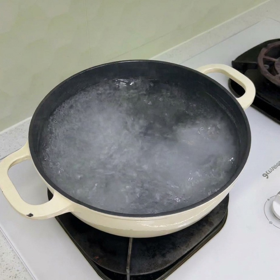 Dry rotini pasta being added to a pot of boiling water.