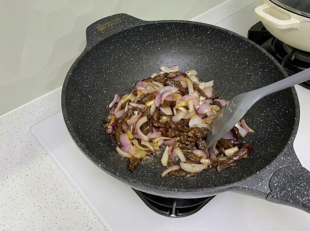 Beef strips and red onions being stir-fried together in a wok.