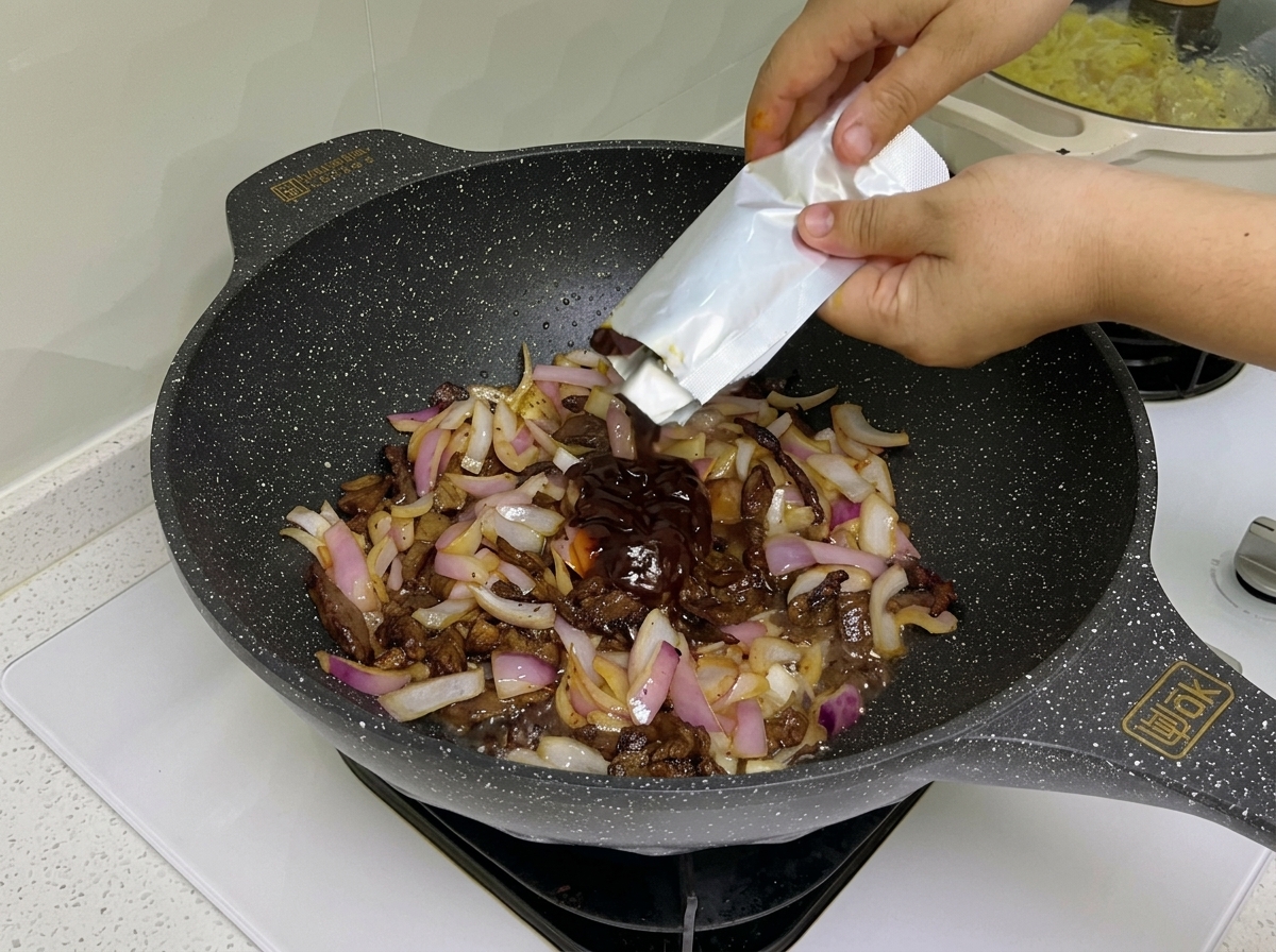 Dark pasta sauce and tomato paste being stirred into a wok containing cooked beef strips and sautéed red onions.