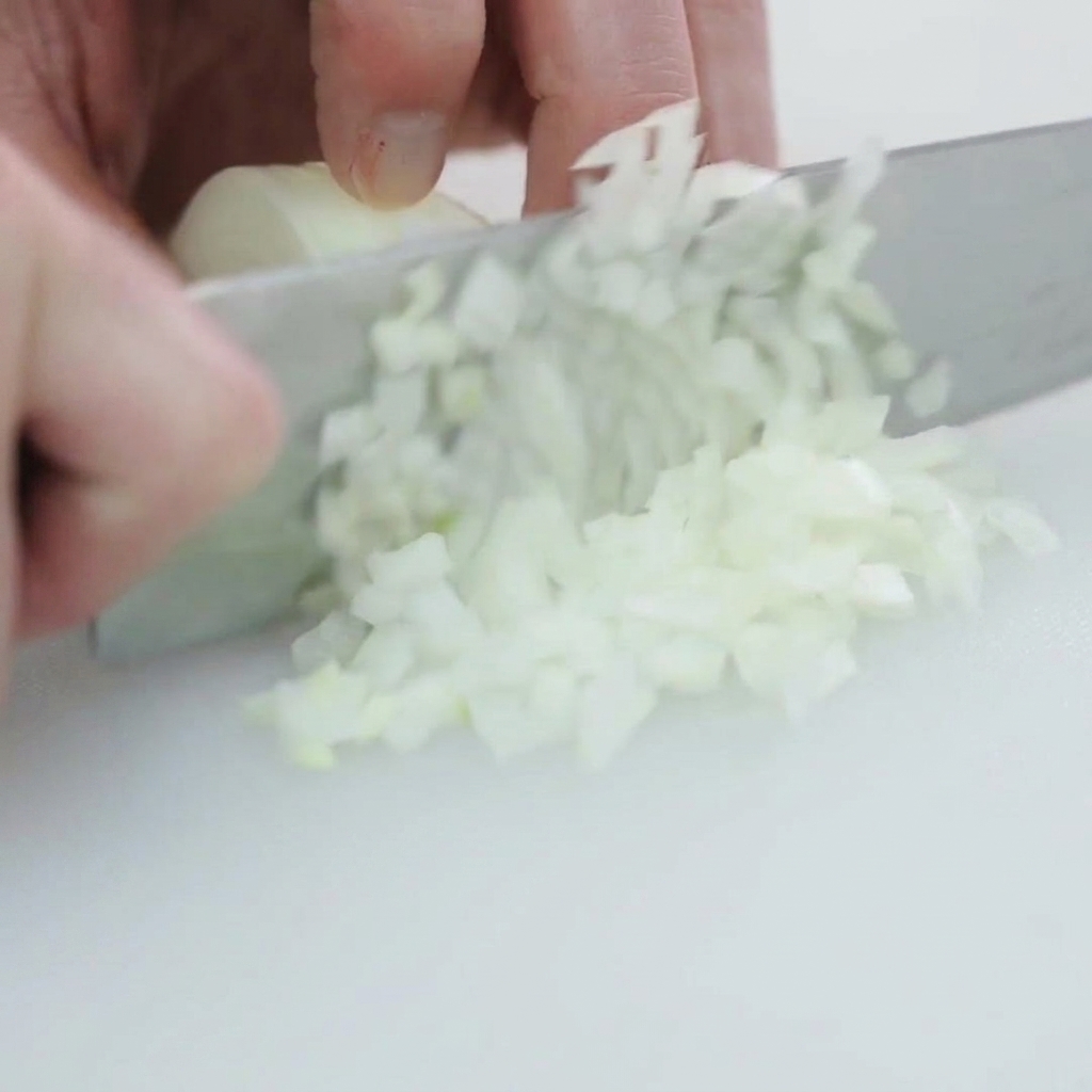 A white onion being diced into small, even pieces on a clean white cutting board.
