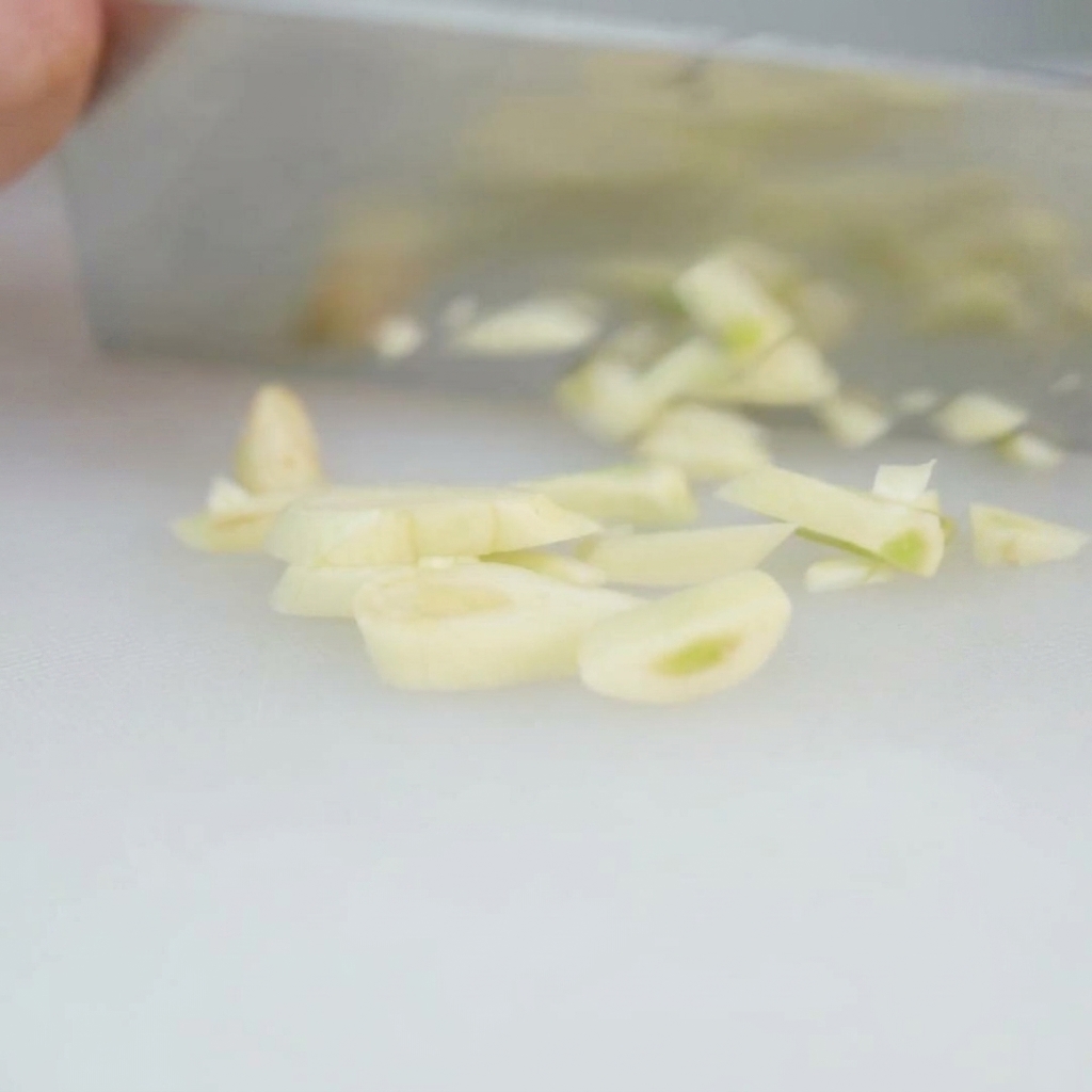 Strips of bacon being cut into small 1 cm pieces and placed into a metal bowl.