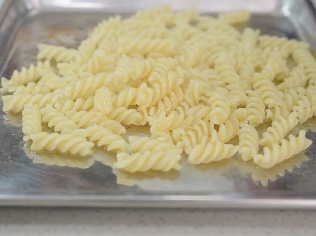 Cooked spiral pasta resting on a metal tray with olive oil drizzled over the top.