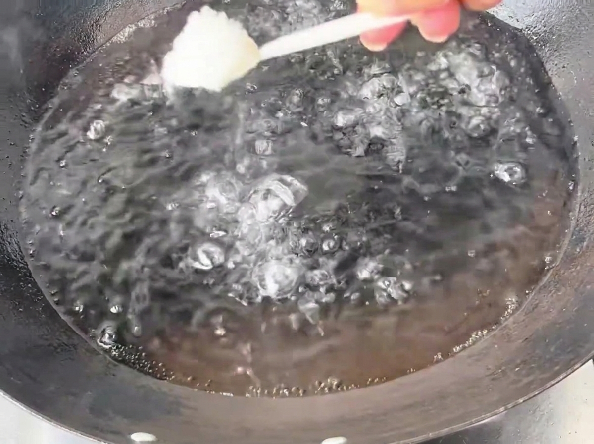 A spoonful of white salt being added into a large iron wok filled with bubbling, boiling water.