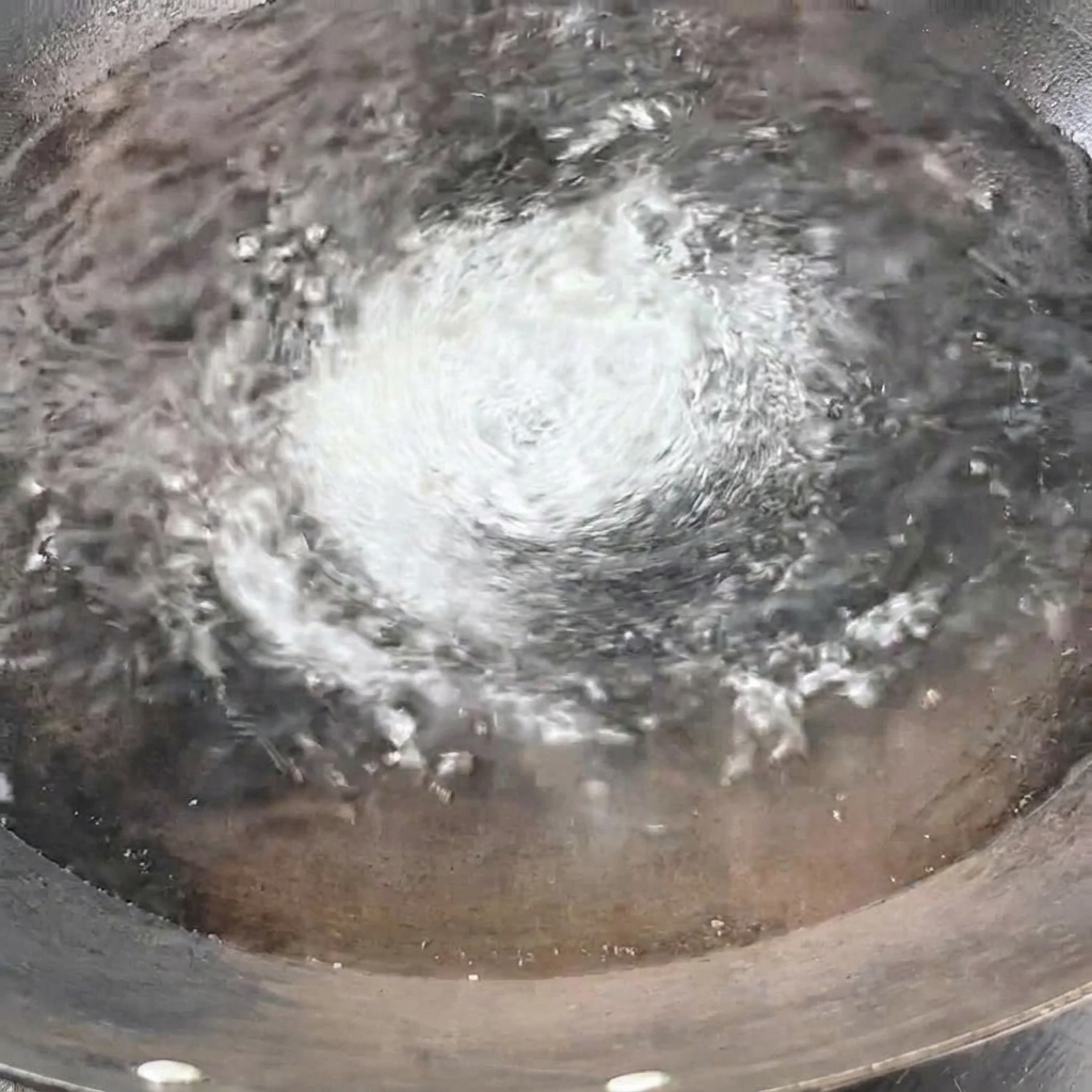 A bundle of dry yellow spaghetti being lowered vertically into the boiling water in the wok.