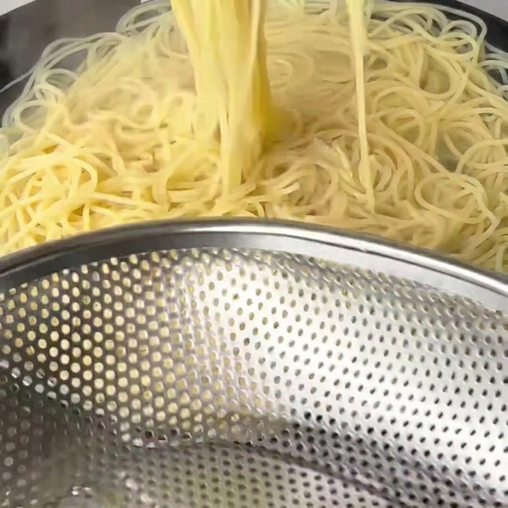Boiled, softened spaghetti noodles being lifted out of the water with long wooden chopsticks.