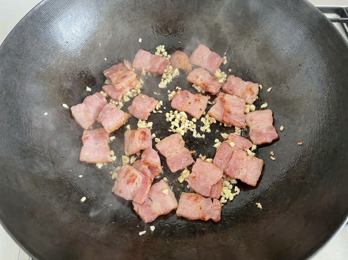 Sliced raw white mushrooms being poured into the wok with the bacon and garlic mixture.