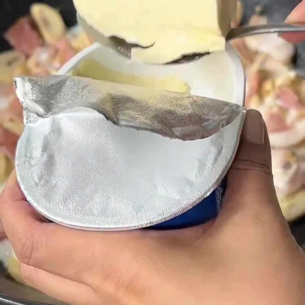 Cream cheese being added to a bubbling milk and vegetable sauce in a wok.