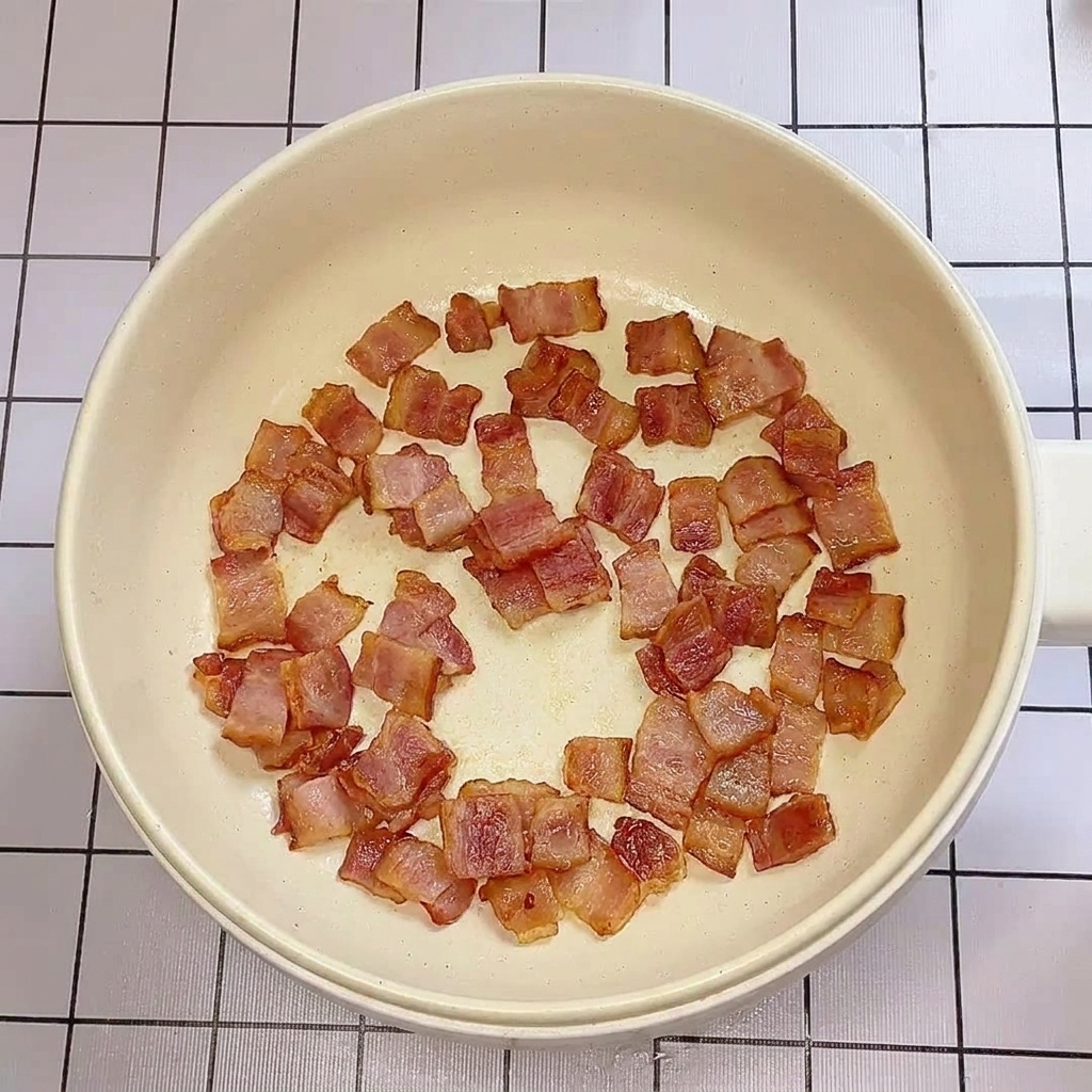 Crispy, browned pieces of bacon cooking in a shallow pan.