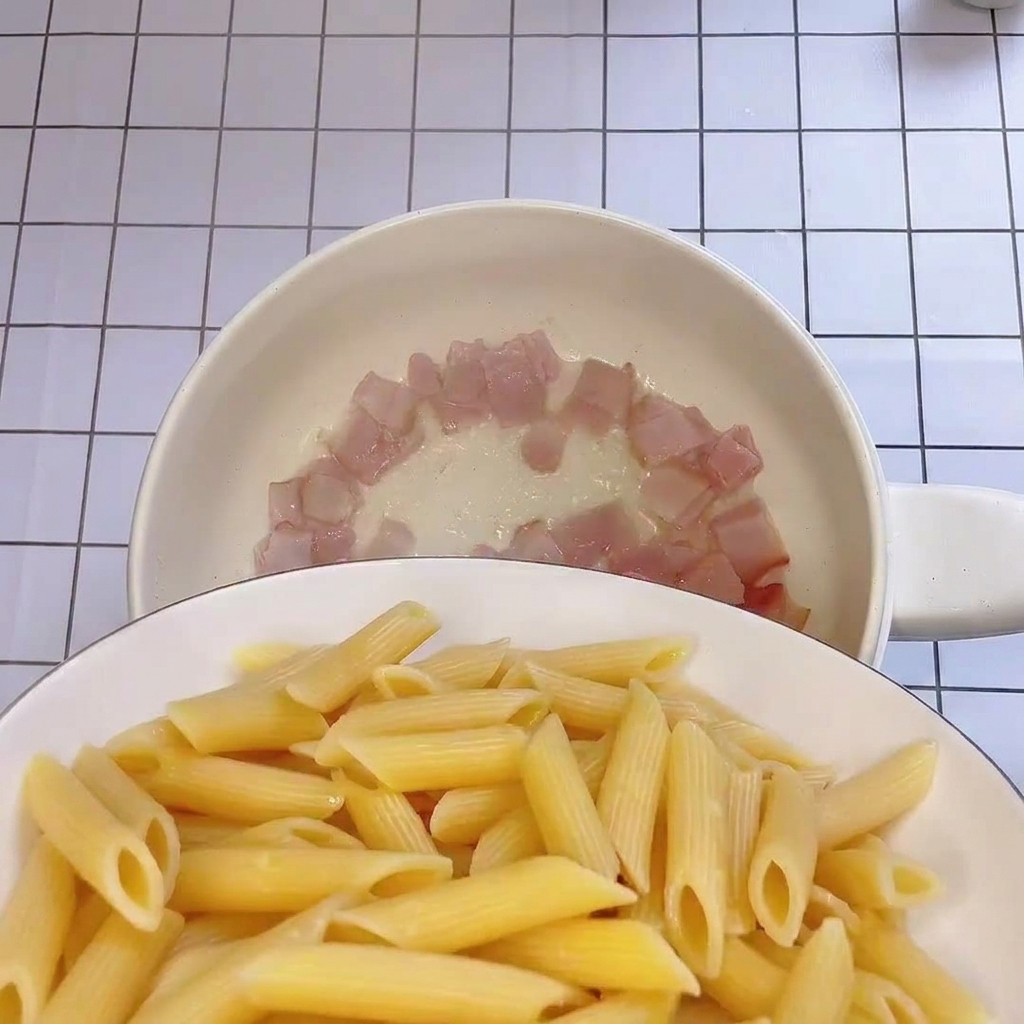 Freshly boiled penne being added to a pan containing crispy bacon bits.