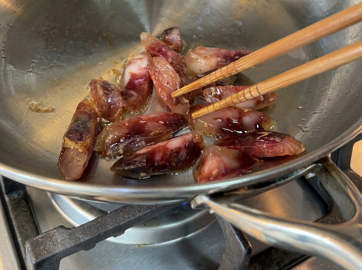 Sausage chunks sizzling in a stainless steel pan with olive oil.