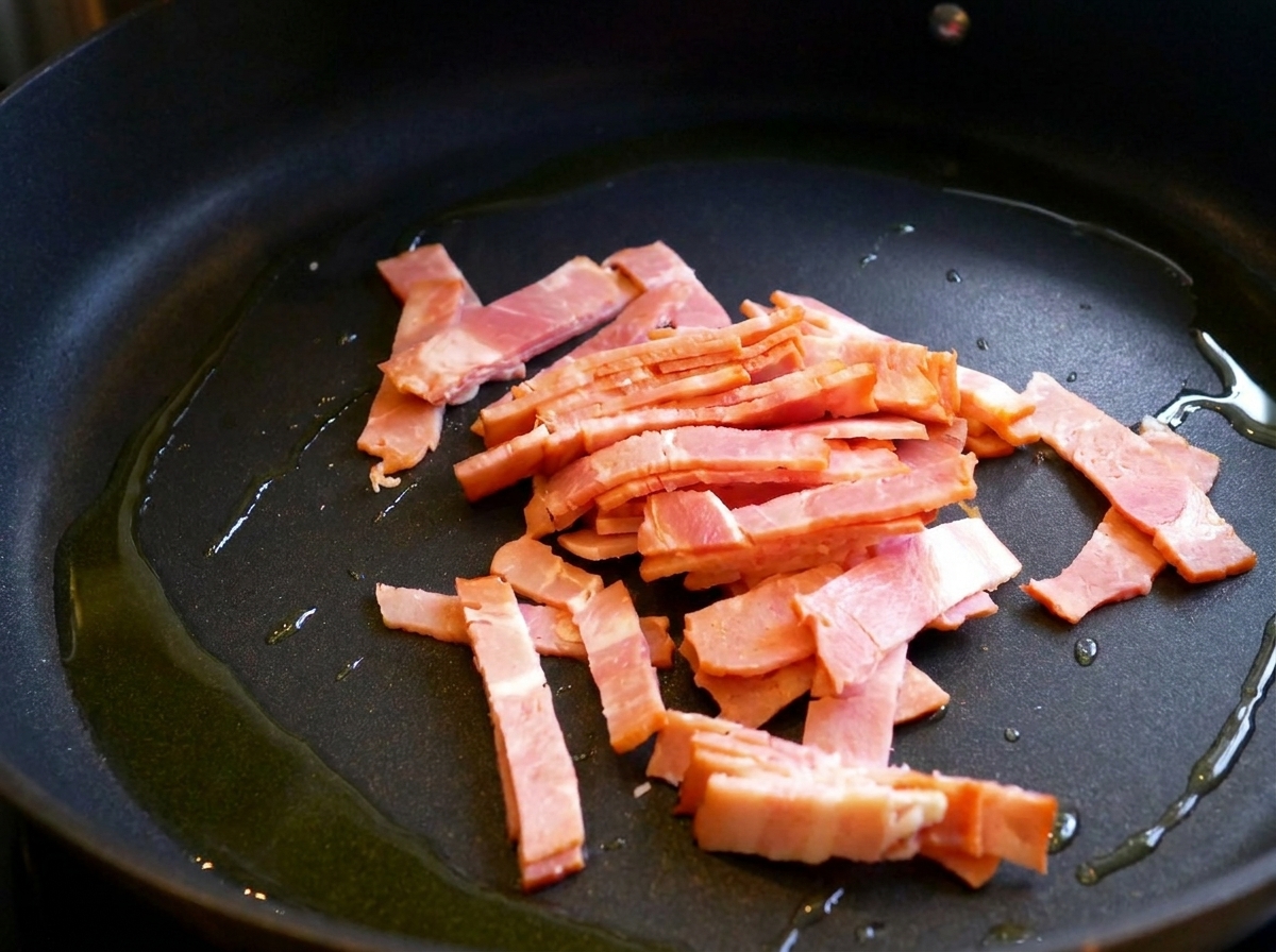 Slices of bacon frying in a skillet with a drizzle of olive oil.