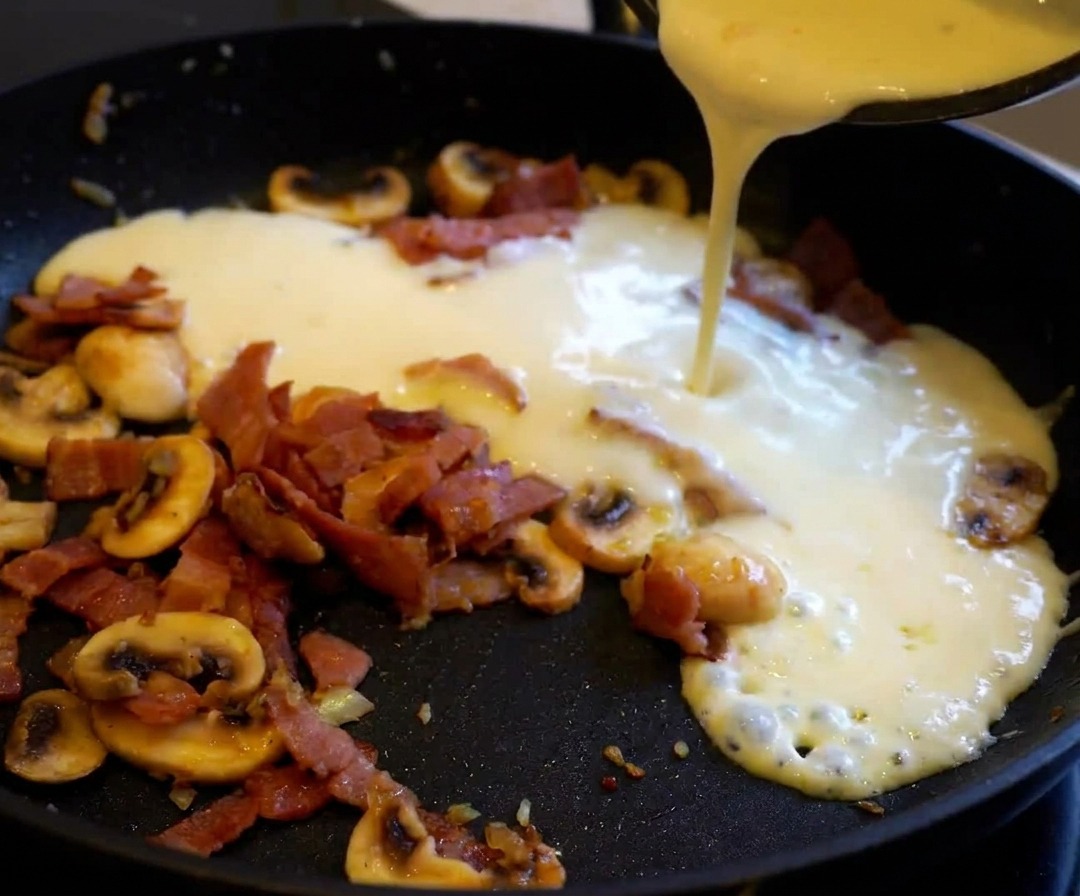 Cooked pasta being added to a pan of creamy bacon and mushroom sauce.