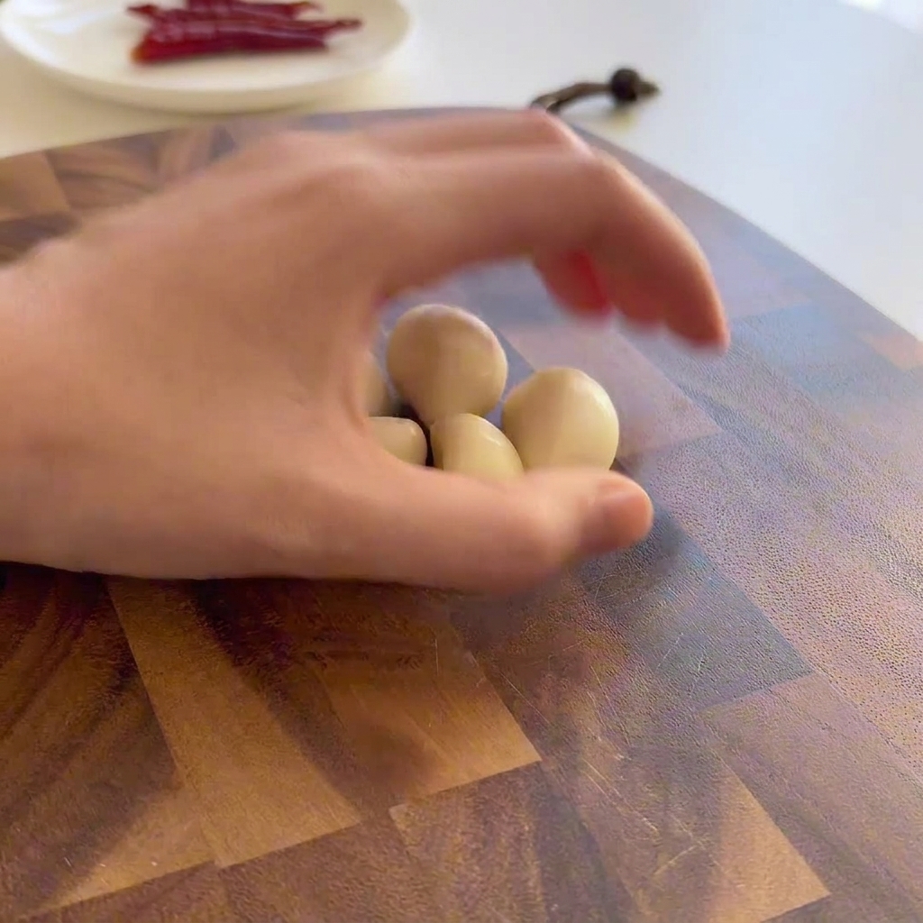 Thickly sliced garlic cloves arranged on a wooden cutting board next to a silver knife.