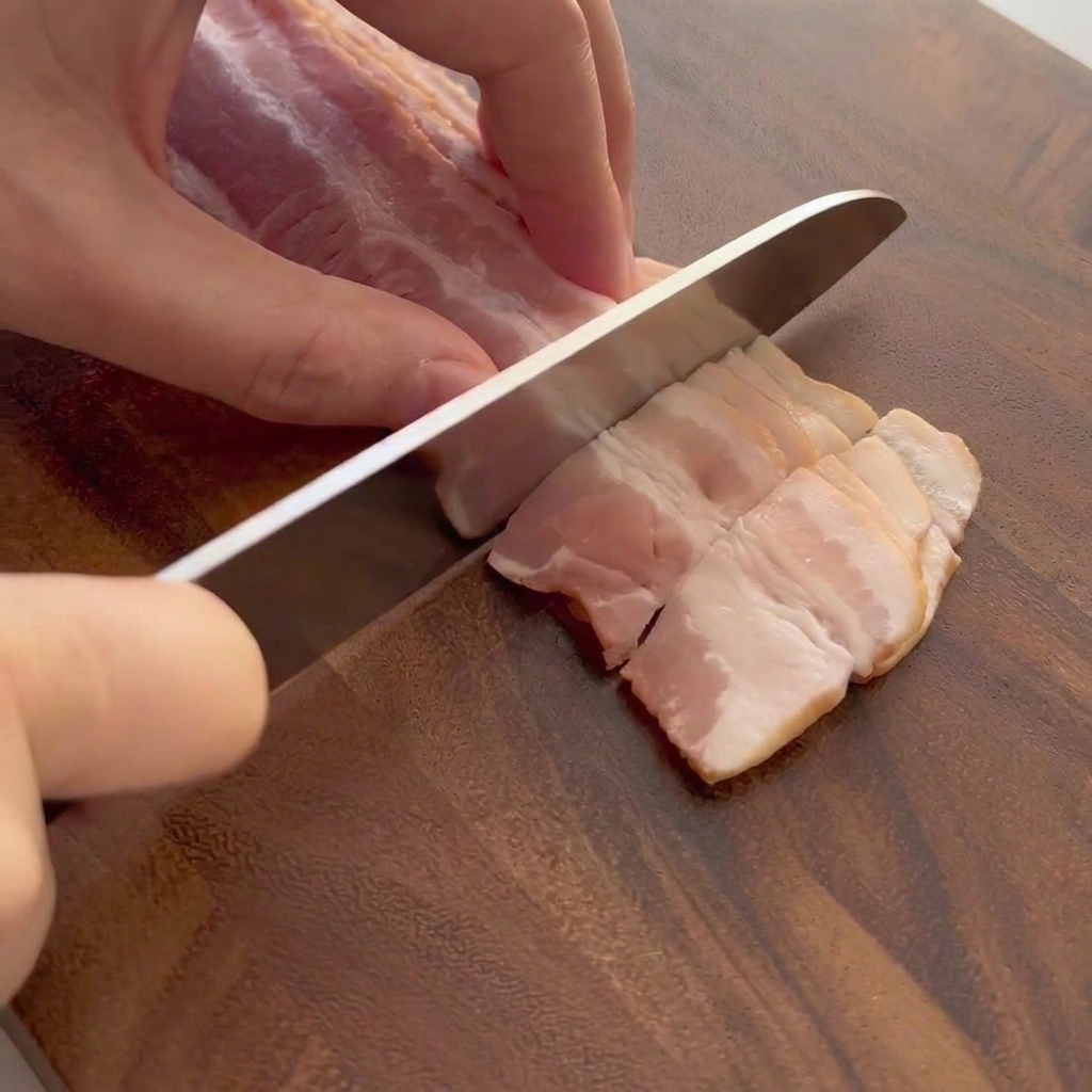 Raw bacon strips being cut on a wooden cutting board.