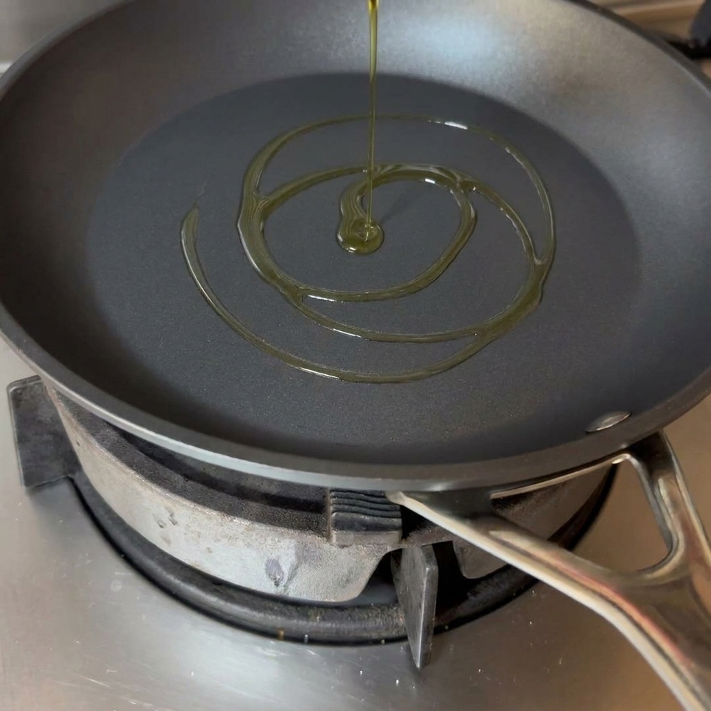 A swirl of golden olive oil settling in the bottom of a black frying pan.