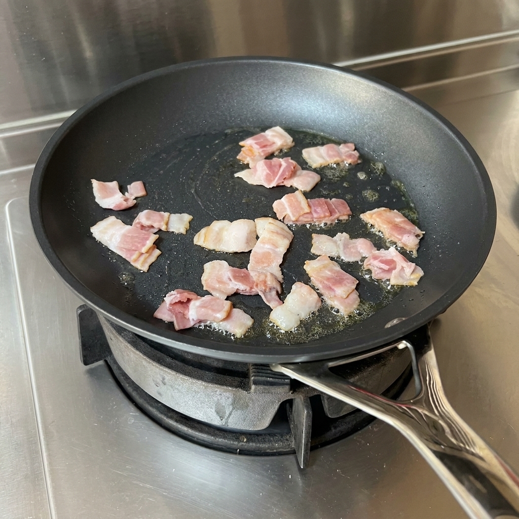 Bacon strips frying in a pan with oil, being stirred by a red spatula.
