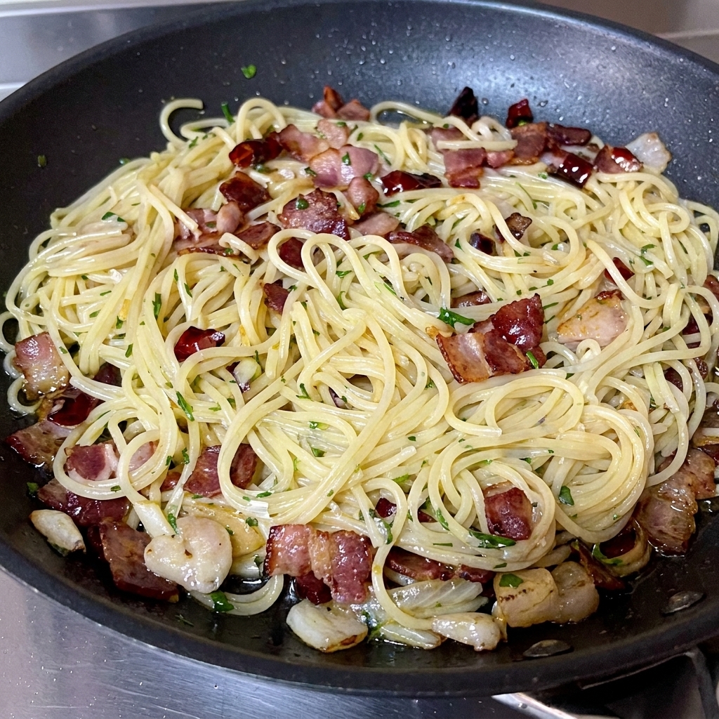Freshly chopped green parsley being sprinkled over a finished pan of spaghetti and bacon.