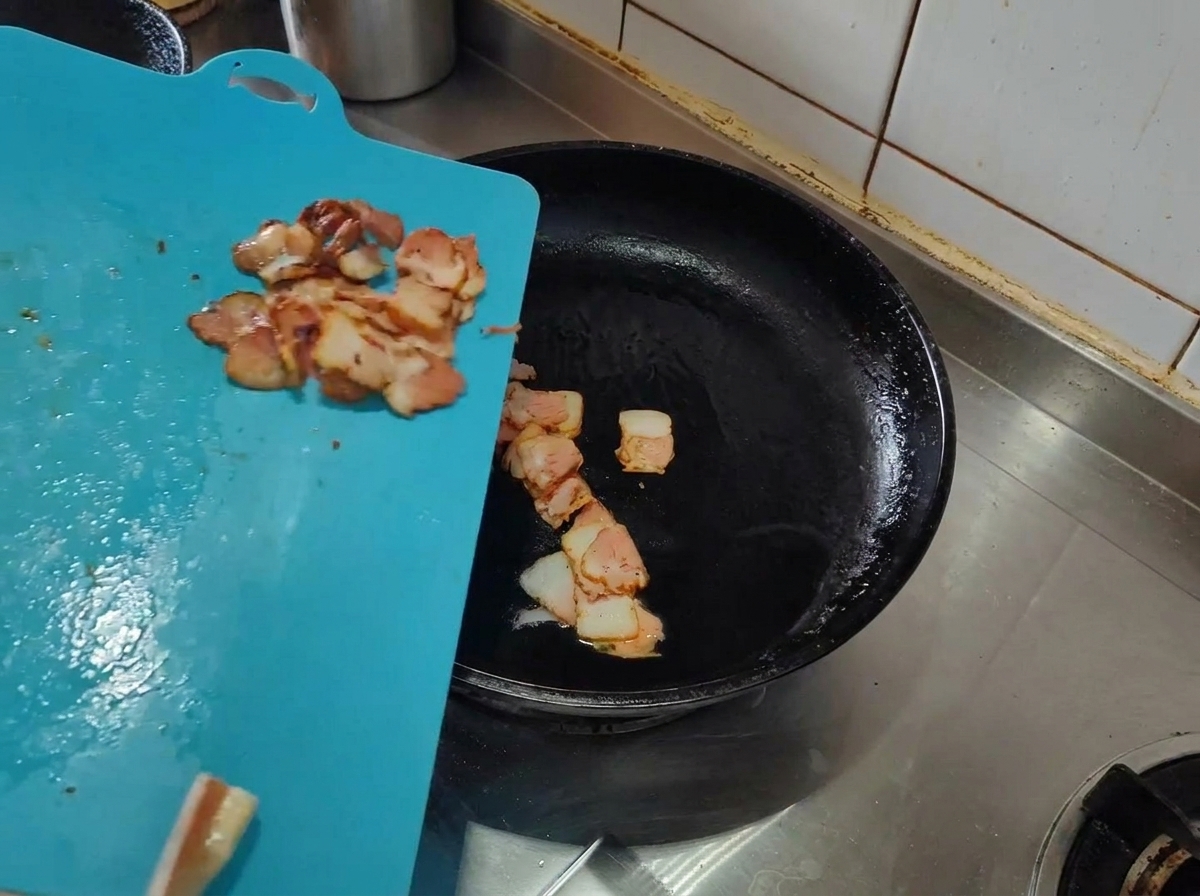 Slices of raw bacon being added to a hot pan with olive oil.