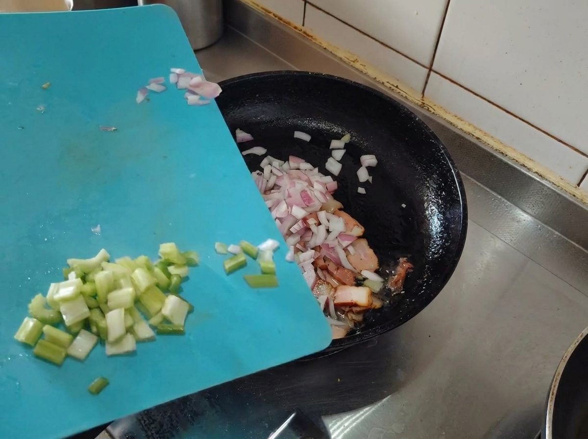 Chopped shallots and celery being added to the pan with browned bacon.