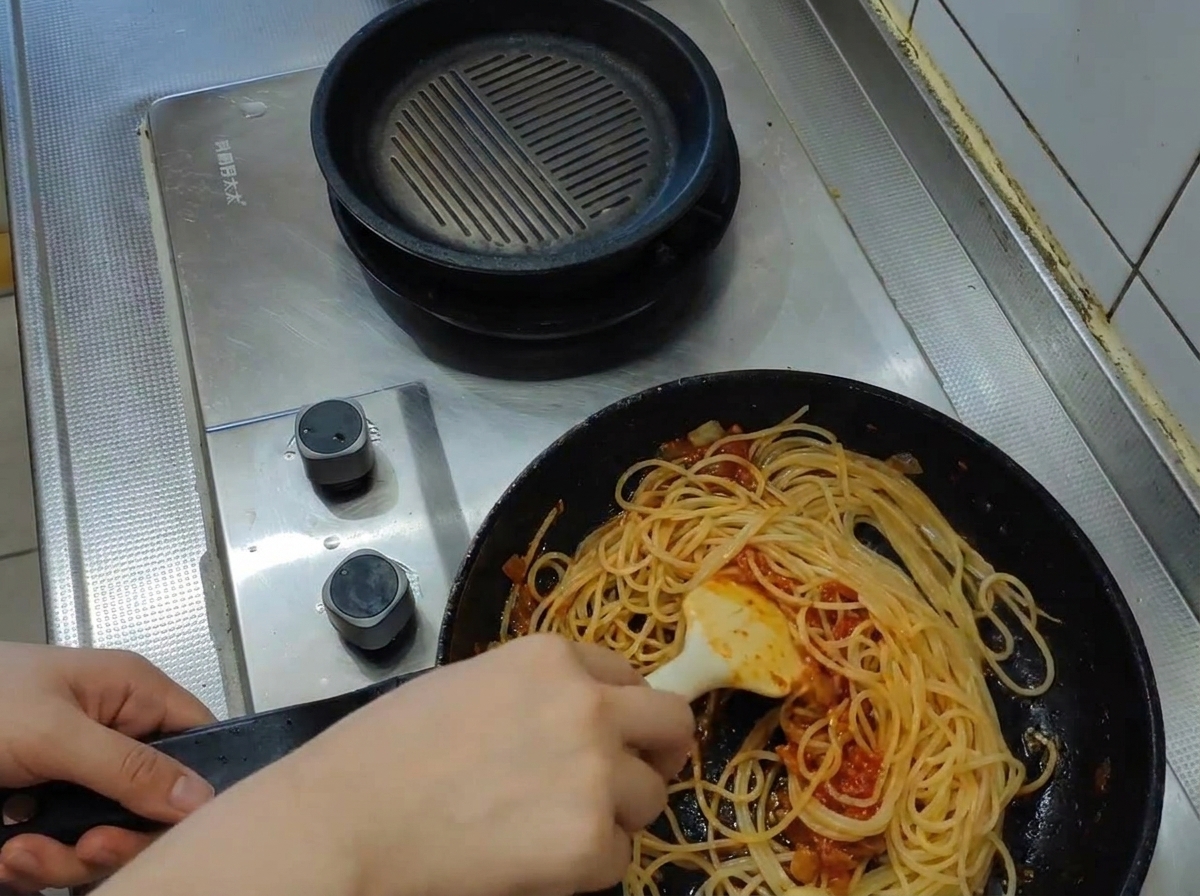 A ladle pouring cloudy, boiling pasta water into a pan filled with spaghetti and tomato sauce.
