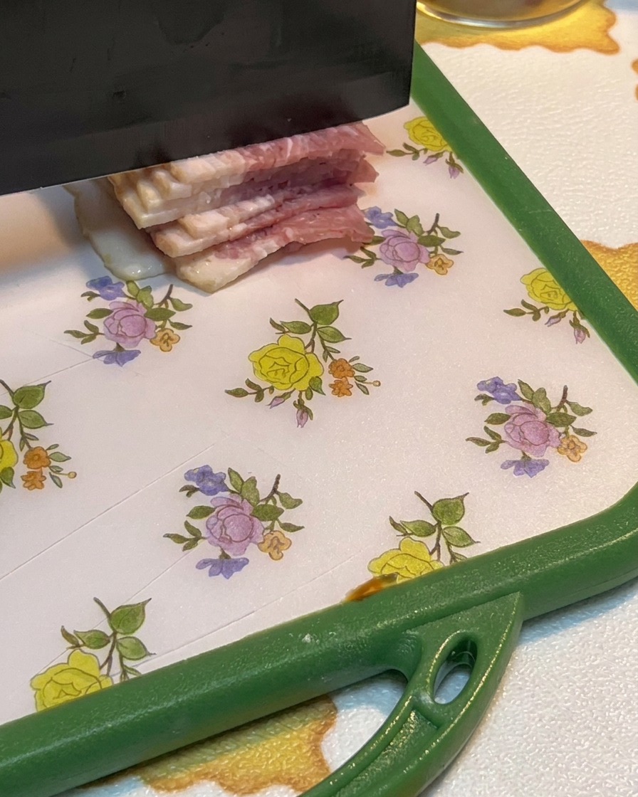 Slices of raw bacon being chopped into small pieces on a cutting board.